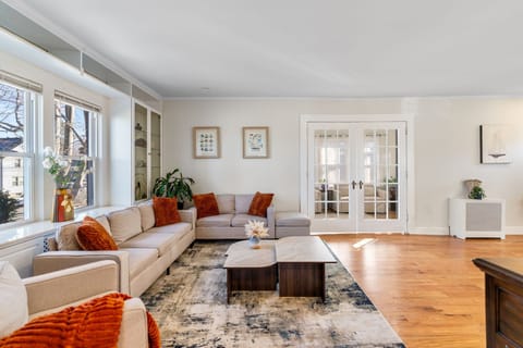 Sun-filled living area with oversized windows overlooking the garden. Neutral tones with warm accent pillows. Calm and inviting atmosphere.