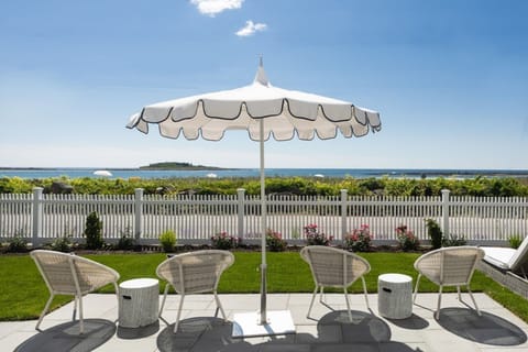 A serene outdoor scene featuring cozy chairs under an umbrella, with breathtaking ocean views just a few steps away.