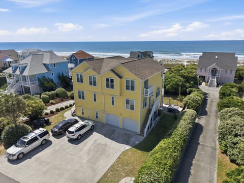 A three-story yellow beachside property nestled in a coastal community, just steps from the ocean with parking and lush landscaping throughout the neighborhood.