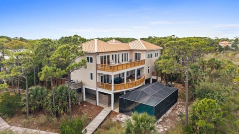 Modern three-story beach house with wraparound decks nestled among coastal palms and native vegetation.