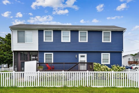 Blue-and-white exterior with lush front landscaping, white picket fence, and steps leading up to the screened porch