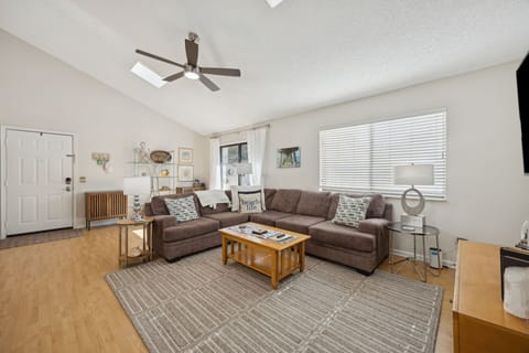 Relax in your comfortable living room with plush sectional seating, ceiling fan, and natural light streaming through large windows.