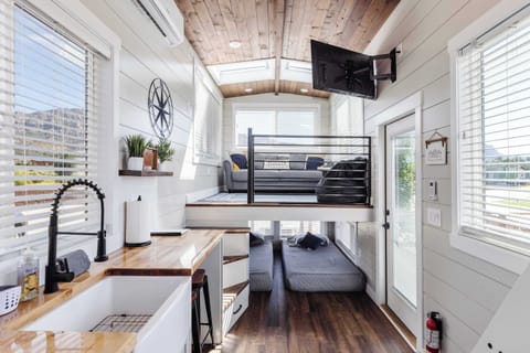 Bright, tiny home living area with abundant natural light, skylights, comfortable seating, TV, and an open layout overlooking the lower sleeping area.