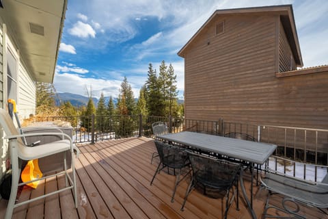 Expansive deck with outdoor dining and breathtaking mountain views surrounded by evergreen forest.