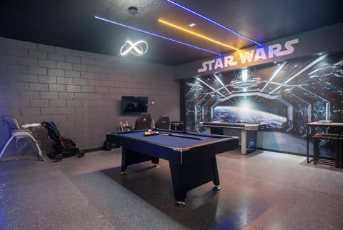 Step into a playful game room featuring a striking Star Wars mural that sets the stage for fun. The sleek pool table invites friendly competition, while vibrant neon lighting adds a dynamic touch to your leisure time.