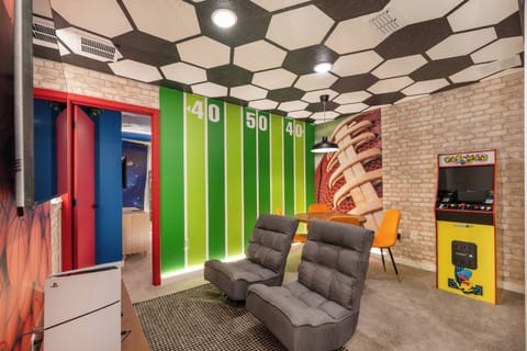 Experience a lively game room with a striking hexagonal ceiling and vibrant colors that energize the atmosphere. Relax in plush gray seating as you enjoy classic arcade games, making it a perfect spot for evenings with friends.