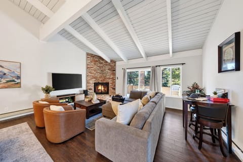Open-concept living room featuring vaulted beamed ceilings, a stone fireplace, and leather armchairs.