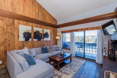 Sink into the plush sectional sofa where warm wood walls and rustic beams create your perfect mountain retreat ambiance.