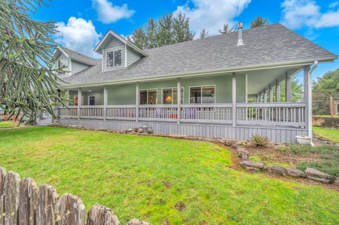 Charming green cottage with wraparound porch and spacious lawn offers peaceful retreat under blue skies.