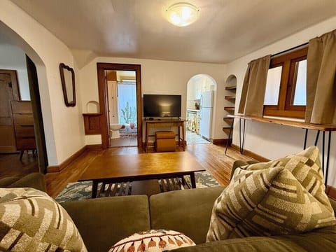 Living Room looking towards the Kitchen (right archway), Full bathroom (left of TV), and Bedroom (left archway).