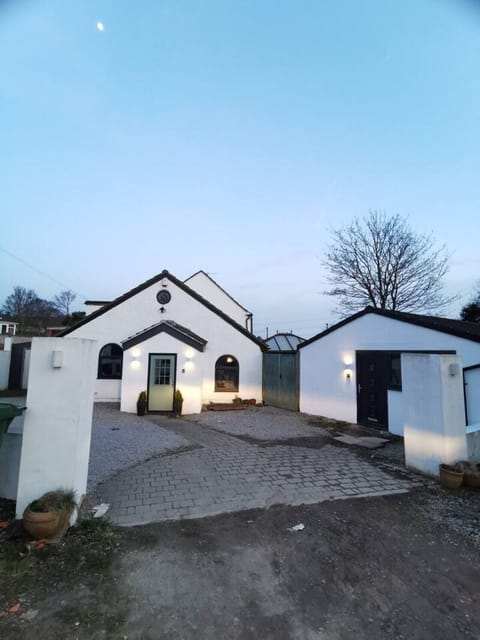 White outbuilding and neighbouring buildings with a shared driveway and paved parking area.