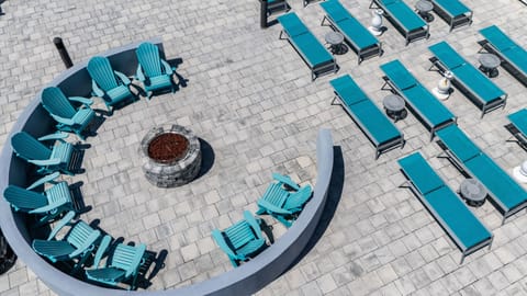 From above, an inviting circle of teal chairs encircles a fire pit, complemented by rows of lounge chairs, creating a perfect gathering space for sunbathing or stargazing.