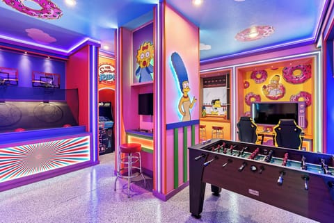 Enter a lively entertainment room adorned with colorful murals and fun games like foosball and basketball arcade, all set against glowing lights for an energetic atmosphere, making it ideal for enjoyable evenings.