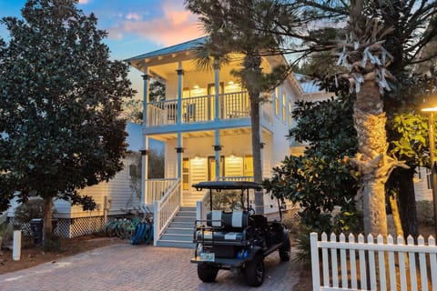 Charming coastal cottage with warm evening lighting creates a welcoming arrival, complete with palm trees and golf cart for easy island exploration.