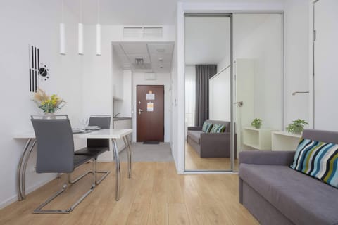 A view from the living area towards the apartment entrance and kitchenette, highlighting the open-plan layout. The clean white walls and light wood-patterned flooring create a cohesive and modern atmosphere.