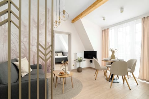 A bright dining area with a round table and upholstered chairs placed near tall windows. Light wood flooring and soft curtains create an airy feel. The space looks elegant and welcoming.