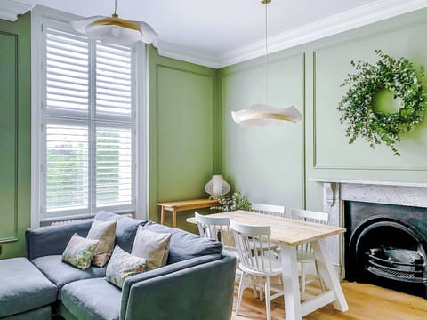 Muted tones, wood floors, and decorative fireplace set a refined tone. Dining table, cozy sofa, and natural light enhance the inviting, stylish atmosphere designed for relaxation and gatherings.