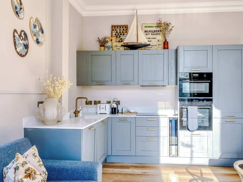 A light‑blue kitchen with white countertops, built‑in oven and microwave, plus toaster, kettle, and coffee machine. Decorative accents and natural light create a warm, welcoming space perfect for guests.