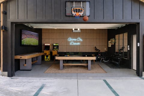 Heated garage game room with pool table, shuffleboard, arcade games, TV, and home gym—an all-season hangout built for groups and families staying in Denver.