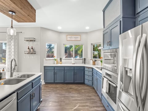 Bright chef-style kitchen with custom blue cabinetry, stainless steel appliances, sleek quartz countertops, and generous prep space—designed for effortless entertaining and elevated vacation living.