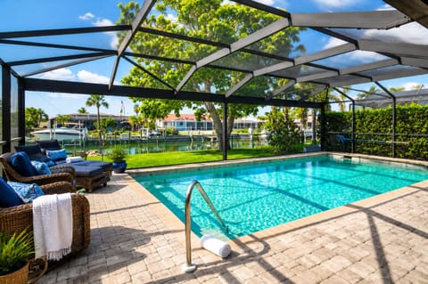 Large outdoor living space with dining table that seats 4, sun loungers, BBQ grill, sparkling pool, and 40-inch Smart TV