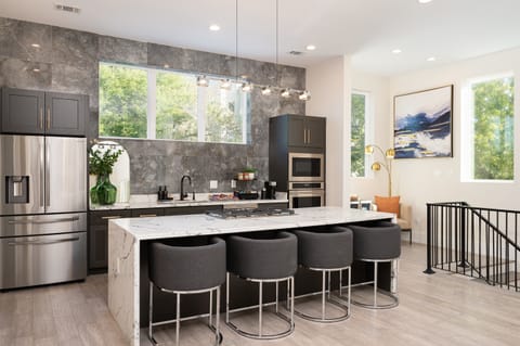 A modern kitchen with a large island, a stainless steel refrigerator, and Monogram appliances including stovetop, oven, microwave and dishwasher.