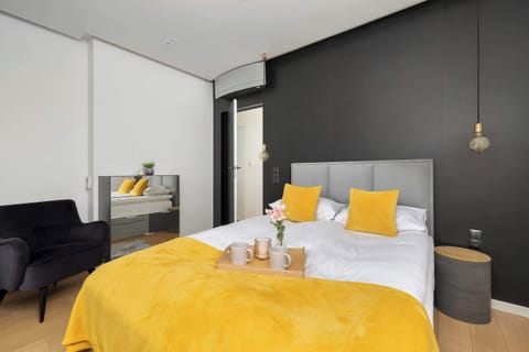 A modern bedroom with a double bed dressed in bright yellow bedding, dark accent walls, and minimalist bedside lighting creating a cozy but stylish atmosphere.