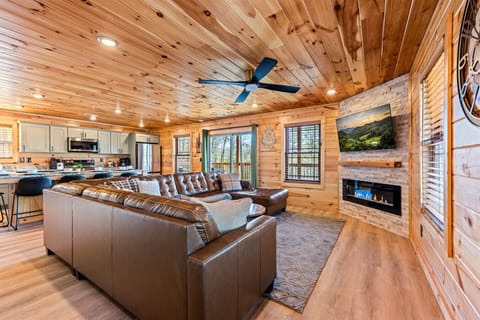 Relax in the open living space featuring a leather sectional, stone fireplace, and fully equipped kitchen. It’s the perfect place to gather, cook, and reconnect after a day exploring the Smokies.
