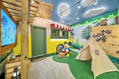 Discover a whimsical playroom filled with vibrant colors and playful decor, featuring a cozy tent and a charming Mickey Mouse. Unique wall art and soft green turf create a delightful space for family fun and memorable moments.