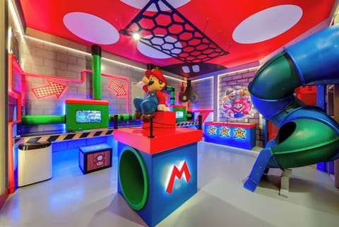 Welcome to a vibrant playroom filled with fun! Enjoy the bold red and blue accents, a playful Mario centerpiece, and an exciting slide. Bright lighting enhances the colorful decor, creating an energetic atmosphere for all ages.