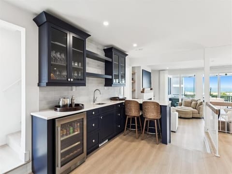 The modern kitchen, adorned with sleek cabinetry and a stylish breakfast bar, exudes elegance while providing a welcoming space for gatherings with ocean views in the background.