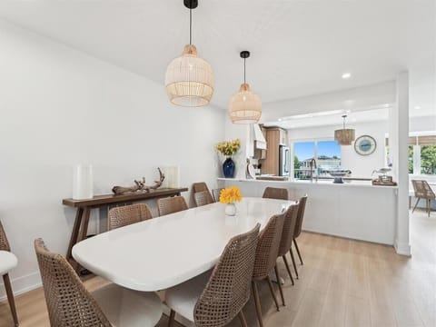 The spacious dining area is bathed in natural light from large windows, featuring a contemporary white table surrounded by stylish woven chairs, perfect for large family gatherings.