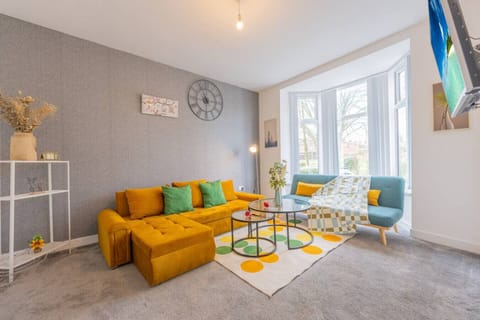 Open living space showing the mustard sofa, coffee table, and a second seating area by the bay window.