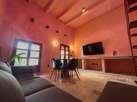 Living room with textured pink walls, patterned tile floor, black dining chairs, and wall-mounted TV.