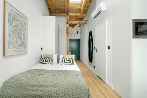 A cozy bedroom area features a comfortable double bed with neutral linens and decorative pillows. Soft lighting and a framed minimalist art piece on the wall create a relaxing atmosphere.