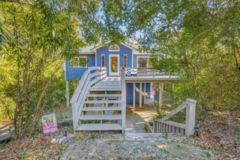 Charming blue cottage nestled among lush trees with wooden walkway leading to elevated entrance.