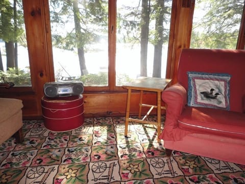 Relax in your cozy lakefront living room, where panoramic windows frame stunning water views and comfortable red seating invites peaceful moments.