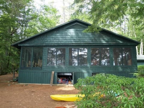 Charming forest cabin nestled among towering trees, featuring large windows and outdoor adventure gear including a bright yellow kayak.
