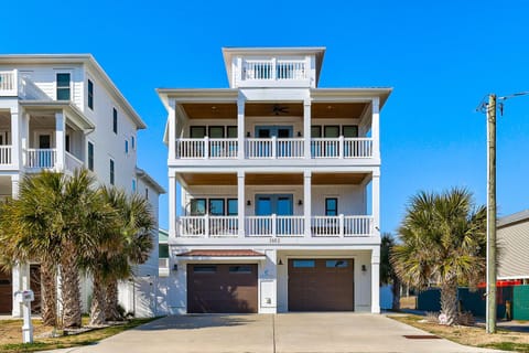 Coastal three-story vacation home with multiple balconies and garage parking in a sunny beachside neighborhood.
