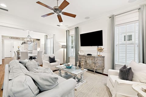 Sink into plush sofas in your elegant living room, where coastal charm meets modern comfort beneath a gentle ceiling fan breeze.