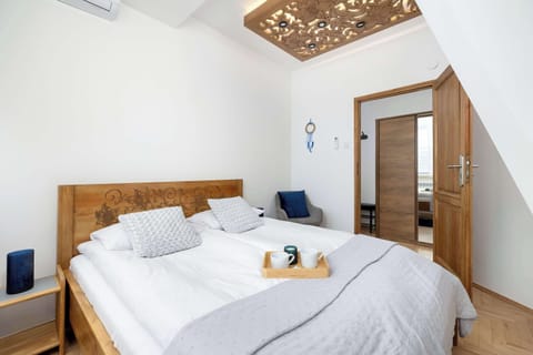 A view of a cozy bedroom with a large double bed covered with white sheets and a gray bedspread. The wooden bed frame and light-colored walls create a peaceful atmosphere for relaxation.