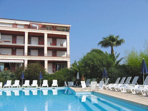 nviting apartment complex with a large outdoor swimming pool, sun loungers, and palm trees under clear blue skies.