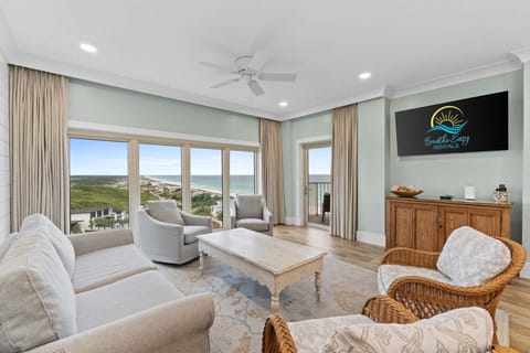 Bright, coastal living room with comfortable seating, Smart TV, and floor-to-ceiling windows leading to a private balcony with stunning Gulf views.