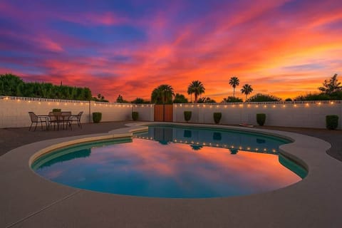 Spacious private backyard oasis featuring a sparkling pool, patio seating and lounging area, string lights, and yard games including giant Jenga, Connect 4, and cornhole, perfect for relaxing and enjoying desert sunsets.