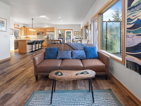 Relax in this stylish living room where natural light streams through large windows, highlighting the leather sofa and artistic touches.