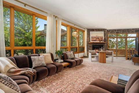 Sink into plush seating while the stone fireplace warms your space and floor-to-ceiling windows frame lush views beyond.