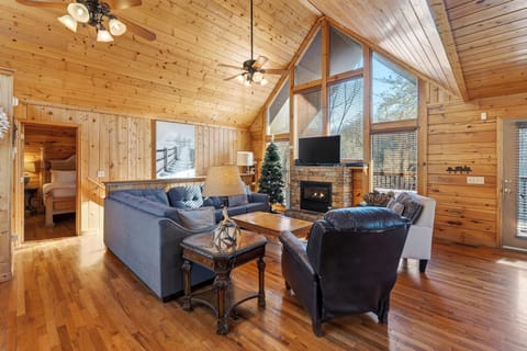 Spacious living room featuring vaulted ceilings, floor-to-ceiling windows, a fireplace, and cozy leather seating.