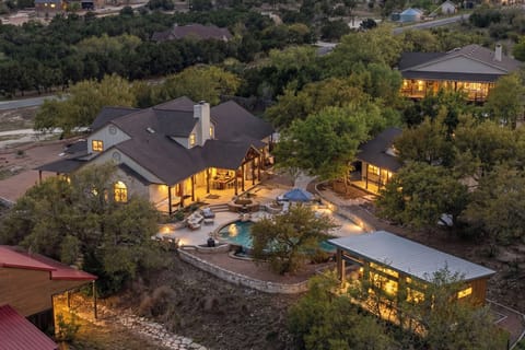 Stunning luxury estate nestled among mature trees with an elegant pool area and beautifully illuminated architecture at dusk.