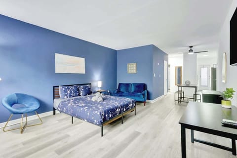 Open space with 1 queen bed, two-seater couch, Smart TV, and workspace under the TV.