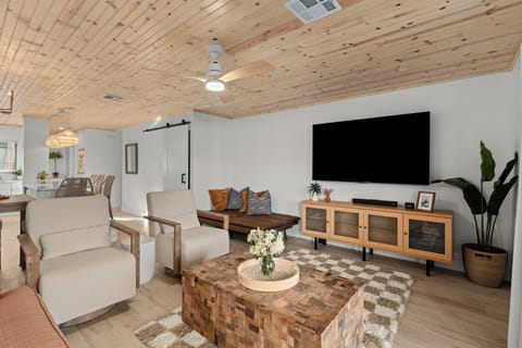 Spacious living room featuring a wood-plank ceiling, wall-mounted TV, and modern coastal decor.